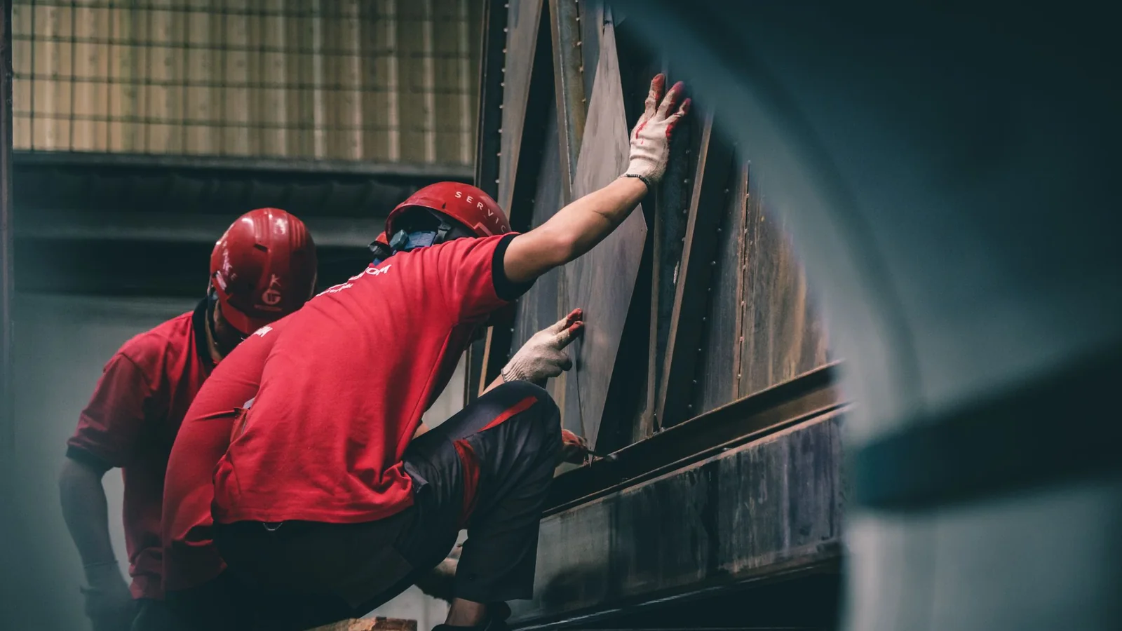 Dos operarios con casco rojo trabajando juntos sobre una estructura metálica en el taller